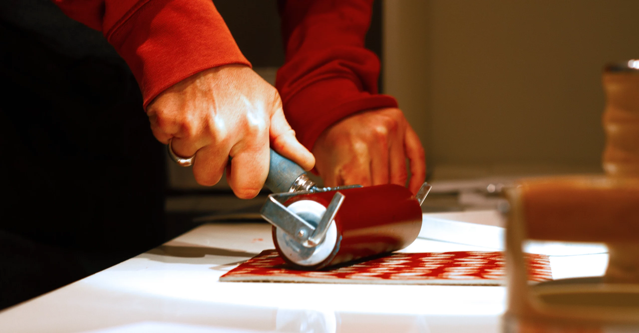 Main d’artiste utilisant un rouleau pour encrer une plaque de lino gravée dans un atelier